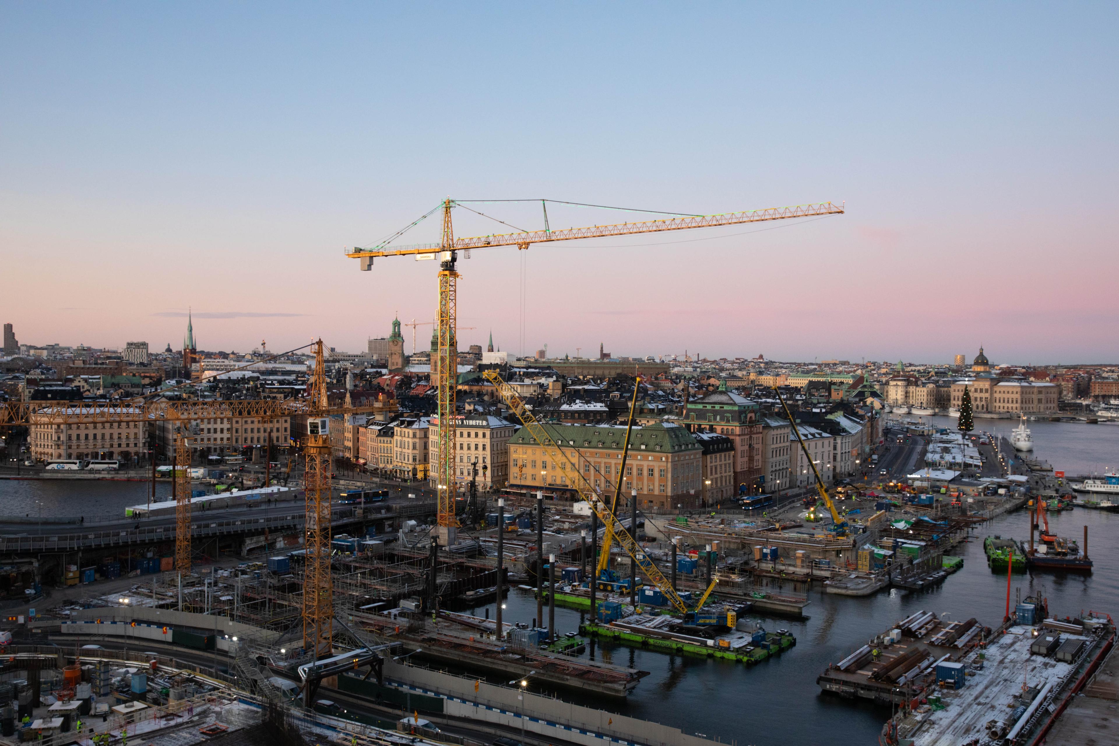 Aerial view of construction sites with cranes and equipment along Stockholm’s waterfront, showcasing the city’s ongoing urban development projects.